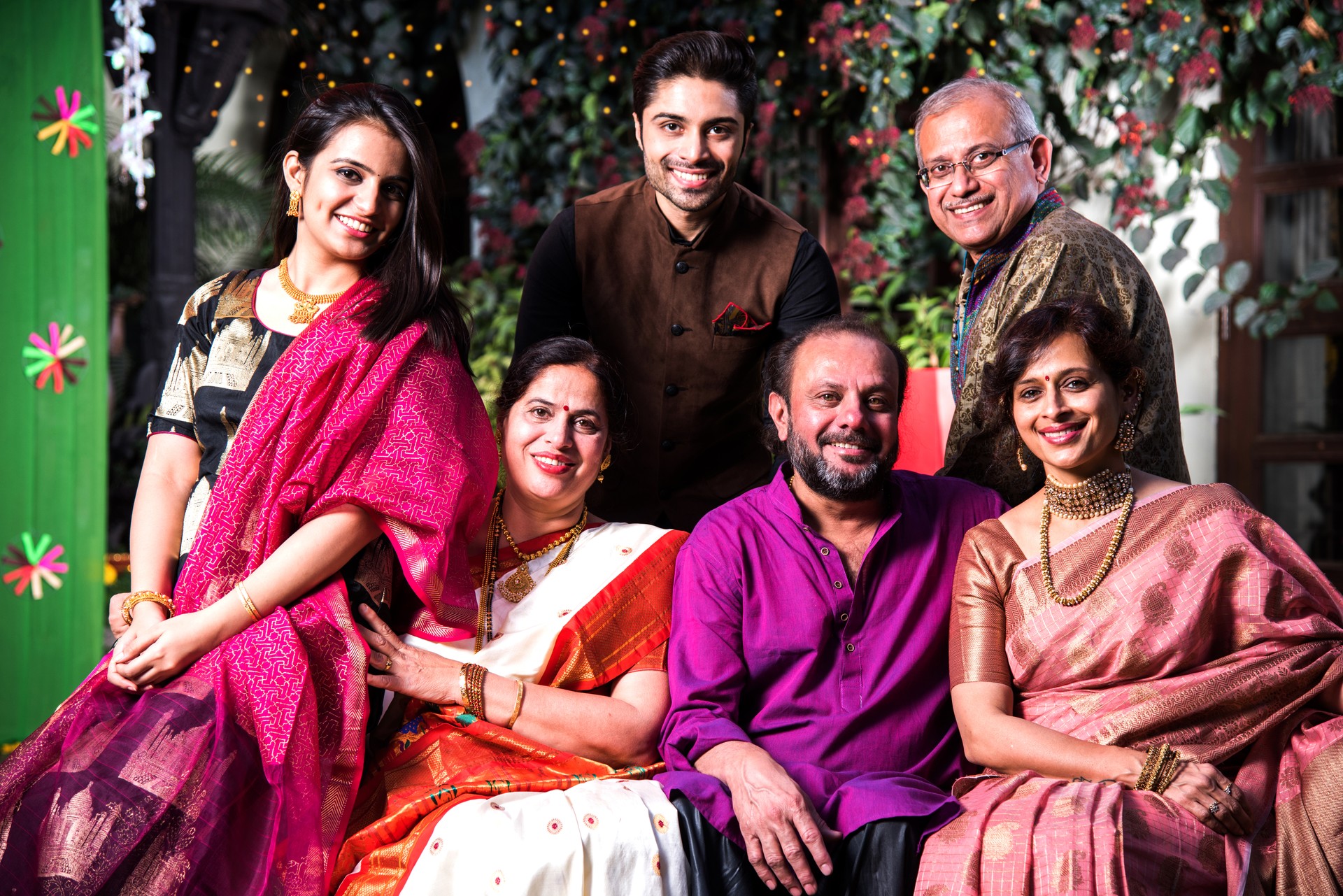 Indian Family posing for group photo on festival or wedding night, sitting on couch or round table with background decorated with colourful frills and lighting series